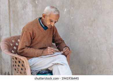 Elderly Man Sitting Alone Writing Diary At Home. Old People Hobby Concept. 