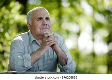 Elderly man sitting in the garden at a wooden table thinking and staring into the distances as he reminisces fond memories, with copyspace - Powered by Shutterstock