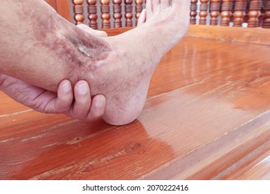 an elderly man sitting on a bench in the house and massaged his ankles which has pain with their own hands to relax