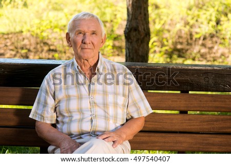 Elderly man sitting on bench. Senior male looking up. Age and wisdom. Quiet day in the park.