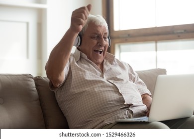 Elderly Man Sitting On Couch Watching Online Sport Match On Pc Scream With Joy Feels Excited Celebrating Football Team Victory, Old Male In Headphones Using Apps Singing Aloud Favourite Song Concept