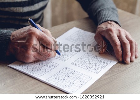 Elderly man solves sudoku or a crossword puzzle to slow the progression of Alzheimer's disease