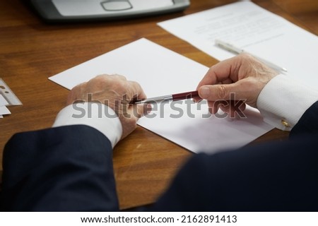 Elderly man in a strict business suit, sitting at a table with a fountain pen, thinks about filling out documents, form or will. The concept of writing a will or filling out forms. No face