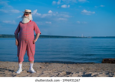 An Elderly Man In A Striped Retro Swim Suit And Boater On The Seashore