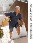 An elderly man struggles to carry groceries up the stairs, showcasing his determination and resilience