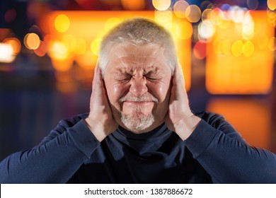 An elderly man suffers from strong noises. He covers his ears with his hands.