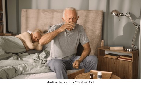 Elderly man taking medication with water in bedroom - Powered by Shutterstock