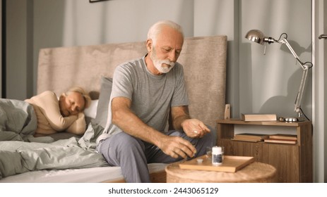 Elderly man taking medication with water in bedroom - Powered by Shutterstock