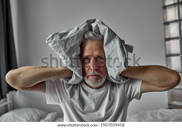 elderly man is tired of hearing\
voices, schizophrenia, closes ears with blanket, at home\
alone