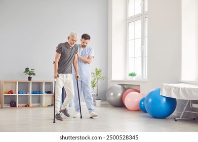 An elderly man undergoes rehabilitation after surgery in a clinic. A male physical therapist helps a patient after a leg injury in a rehabilitation center. - Powered by Shutterstock