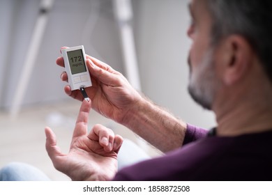 Elderly Man Using Glucometer To Check Blood Sugar Level At Home