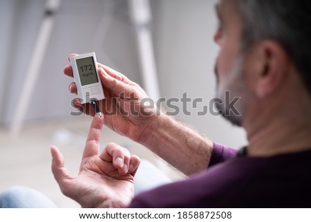 Elderly Man Using Glucometer To Check Blood Sugar Level At Home