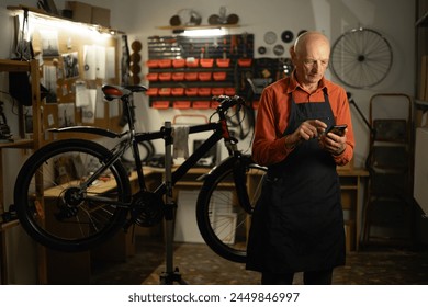 Elderly man using a smartphone in a bicycle repair shop. Copy space - Powered by Shutterstock