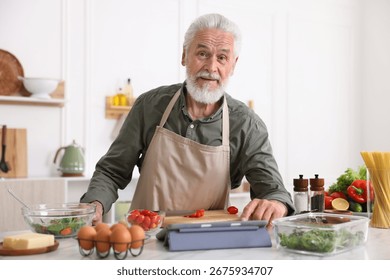 Elderly man using tablet while cooking at white marble table in kitchen