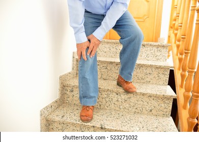 Elderly Man Walking Down The Stairs At Home And Touching His Knee By The Pain