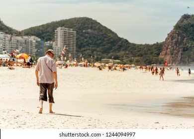 Elderly Man Walking Head Down On Copacabana Beach In Rio De Janeiro, Brazil