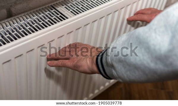 An elderly man warms his hands near a\
heating radiator, a man froze, a man warms himself near a\
fireplace. A man warms himself up by an electric\
battery