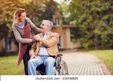 Elderly Man In Wheelchair With Her Cheerful Daughter Enjoying To Visit Together In Sunny Day
