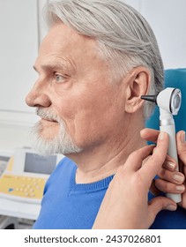 Elderly man while ear test with audiologist with otoscope at medical office, close-up. Diagnosis of hear impairment, check-up, otoscopy