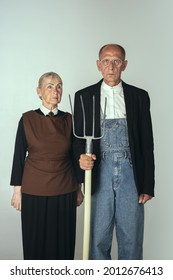 Elderly man and woman in art performance, replica of painting american gothic. Retro style, comparison of eras and cultural concept. Old actor and actress like farmers. Copy space for ad.