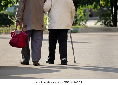 Elderly man and woman with cane walking down the street, rear view. Old couple holding hands together, concept of old age, diseases of the joints and spine - Powered by Shutterstock