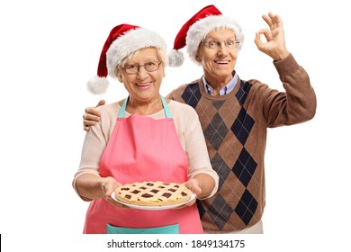 Elderly man and woman with a freshly baked pie wearing christmas hats isolated on white background - Powered by Shutterstock