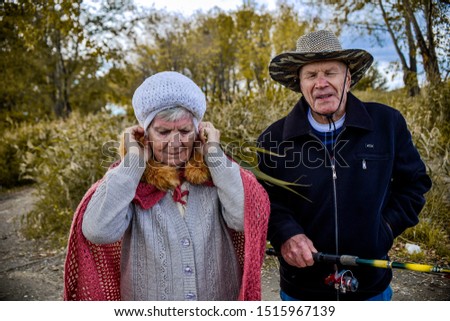 an elderly man and woman are walking by the river in the fall, fishing with a fishing rod and smiling and talking