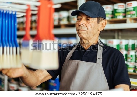 Elderly man working in a hardware store restocking items on shelves. Small business concept.