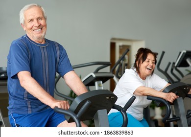 Elderly man working out on exercise bike in gym. Retired caucasian man looking at camera while exercising at fitness club. Training for long living.