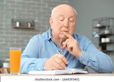 Elderly Man Writing In Notebook At Home