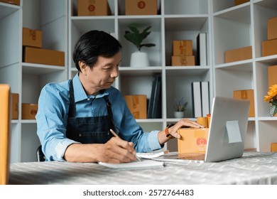 Elderly man writing notes while organizing packages in a modern workspace