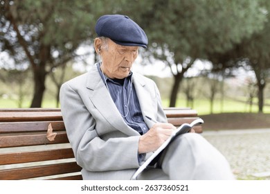 Elderly man writing notes while listening music on park bench