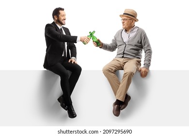 Elderly man and a young businessman sitting on a blank panel and toasting with bottles of beer isolated on white background