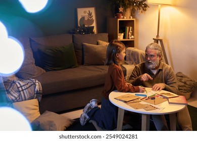 Elderly man and young girl spending quality together time making crafts. Cozy living room decorated with holiday decor and warm ambient lighting creates inviting atmosphere - Powered by Shutterstock