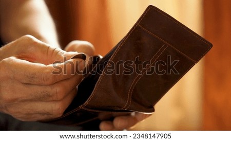 An elderly man's hands, covered with knotted veins, search for coins in his wallet