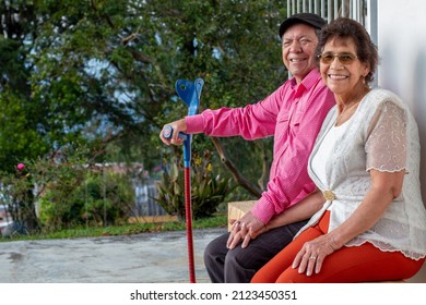 Elderly married couple looking at the camera while smiling. Elderly couple sitting on a wooden bench in the courtyard of their farm in nature.