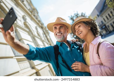 Elderly married couple taking a selfie in the city center. Exploring and traveling concept. They are wearing backpacks and hats. - Powered by Shutterstock