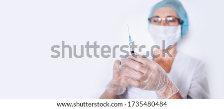 Elderly mature woman doctor or nurse with syringe in a white medical coat, gloves, face mask wearing personal protective equiment isolated. Healthcare and medicine concept. Covid-19 pandemic crisis
