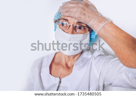Elderly mature woman doctor or nurse arms crossed in a white medical coat, gloves, face mask wearing personal protective equiment isolated. Healthcare and medicine concept. Covid-19 pandemic crisis
