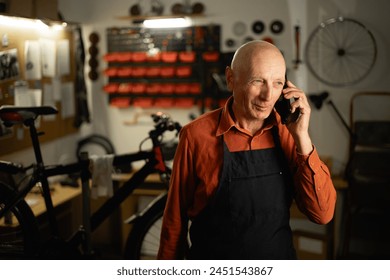 Elderly Mechanic in bicycle workshop using a mobile phone standing near bike. Copy space - Powered by Shutterstock