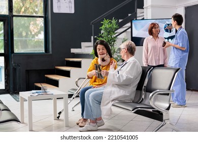 Elderly Medic And Patient With Cervical Neck Collar Looking At Xray Scan Examn, Doing Checkup Visit In Hospital Waiting Room. Asian Woman With Physical Pain And Injury Having Medical Appointment.