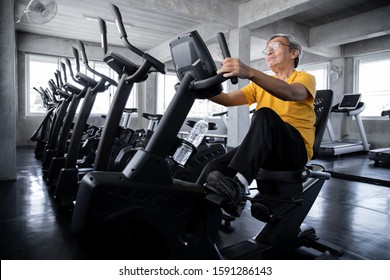 Elderly Men Are Exercising By Spinning The Bike In The Gym. Concept Of Healthy Elderly With Exercise. Asian Mature Men Playing Exercise Machines In The Gym