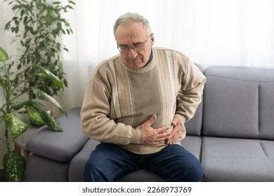 Elderly men have abdominal pain sitting on the sofa in the house. Concept Problems of the digestive tract in older people, health care. - Powered by Shutterstock