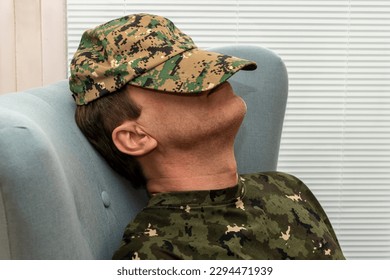 An elderly military man 45-50 years old covered his face with an army cap, sleeping sitting in an armchair. Concept: mental disorders in military personnel, treatment by a psychotherapist. - Powered by Shutterstock