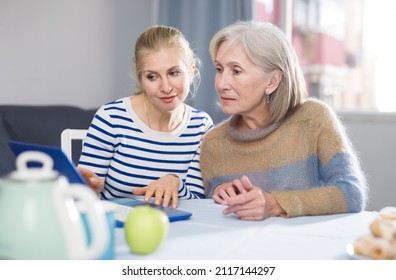 Elderly mother and adult daughter looking at laptop screen at home - Shutterstock ID 2117144297