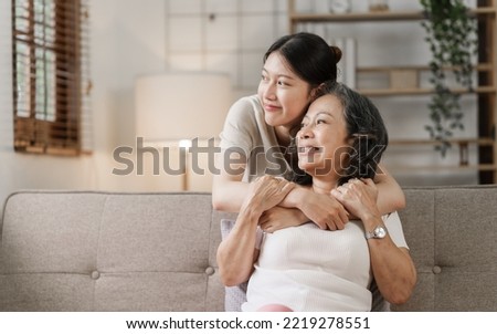 Elderly mother and grown daughter holding hands sitting on the sofa hugging.