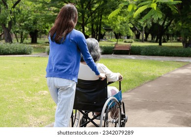 An elderly mother in a wheelchair with her daughter or caregiver. Take a leisurely walk in the park. They are happy. Family concept. health care, life insurance - Powered by Shutterstock