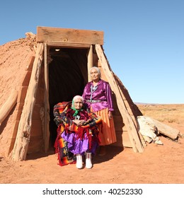 Elderly Native American Women Pose Outside A Tribal Abode. They Are Full Length Viewable And Looking At The Camera. Squarely Framed Shot.