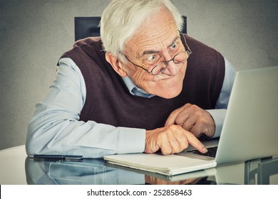 Elderly old man using computer sitting at table isolated on grey wall background. Senior people and technology concept 