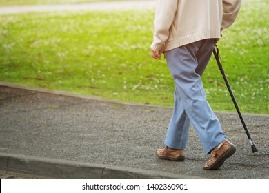 elderly old man with walking stick stand on footpath sidewalk crossing the street alone roadside in public park. concept senior across the street. soft focus